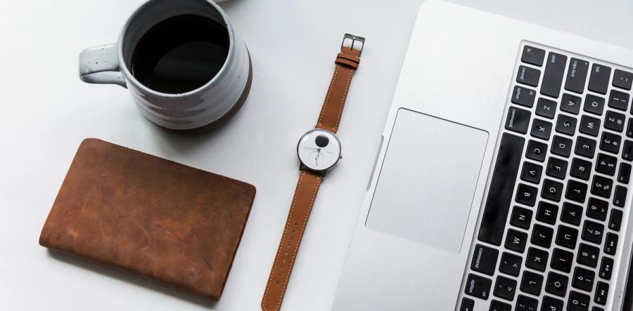 A Withings watch on a desk beside a notebook and coffee