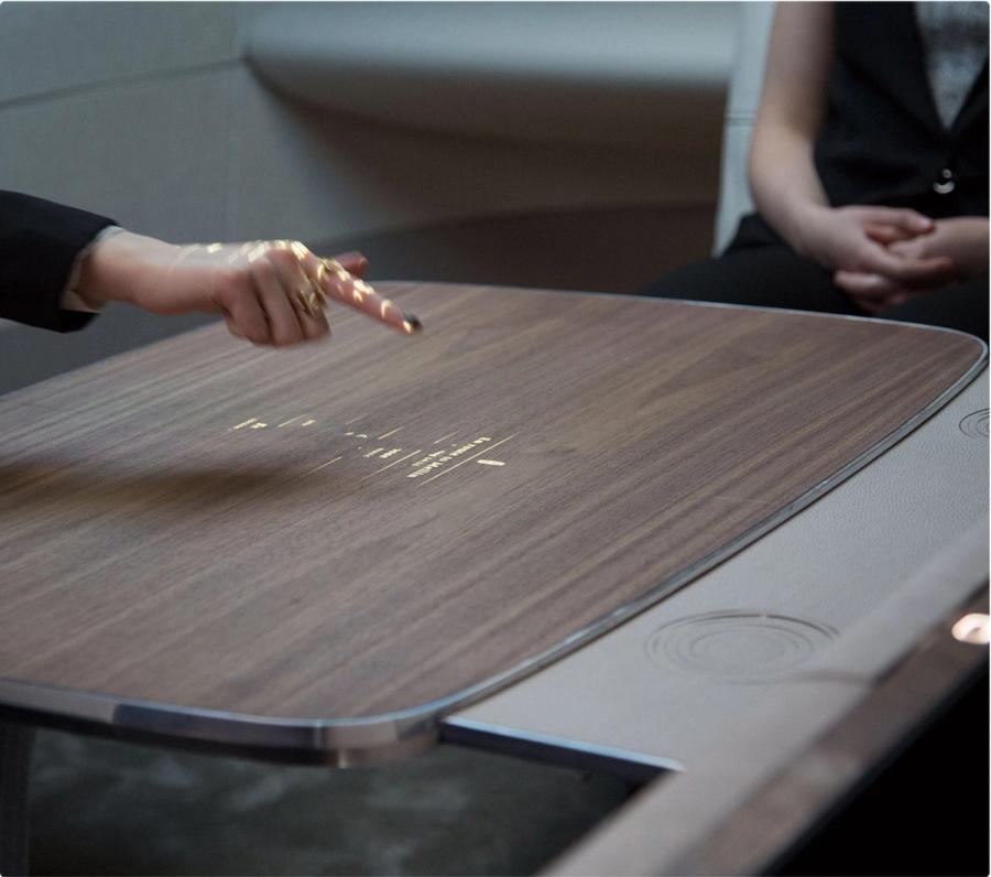 A hand reaching for the walnut table in Ford’s autonomous vehicle simulator, its interface projected onto the wood