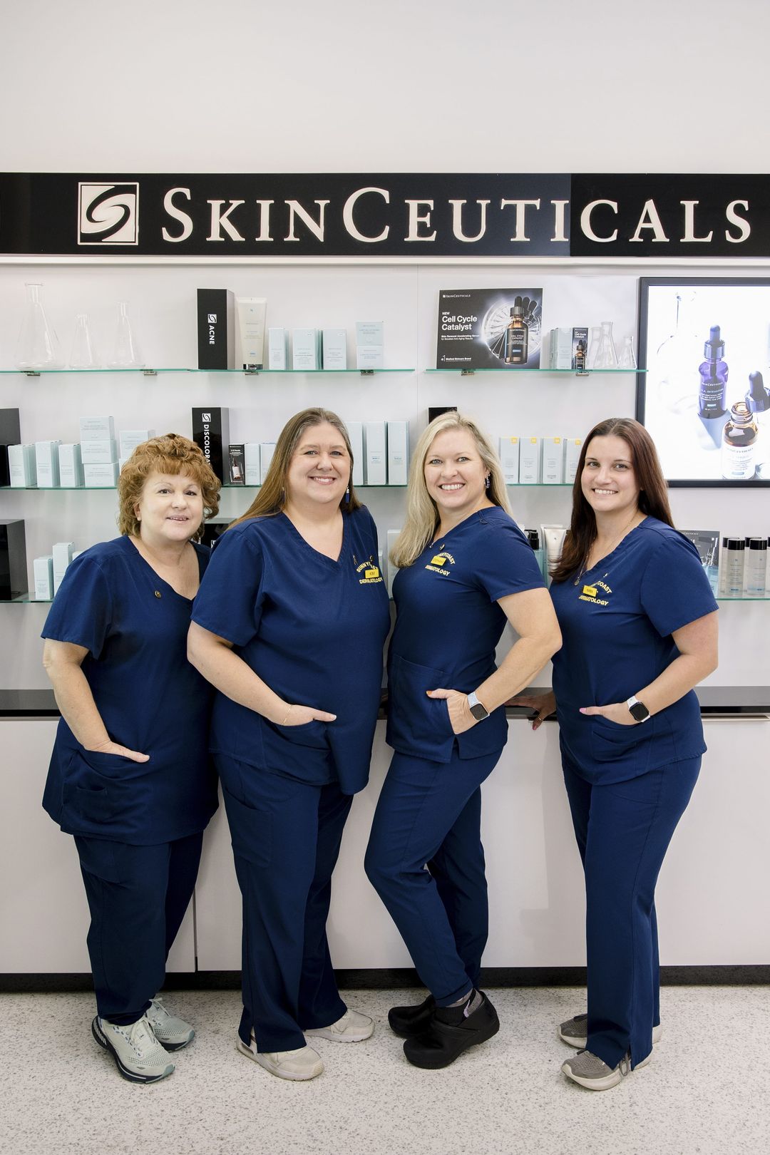 Sunnycoast Dermatology front-office staff in navy scrubs by the SkinCeuticals display