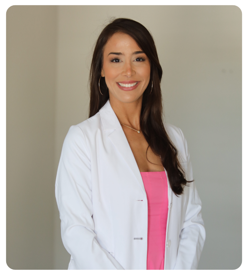 Keely Chandler in a white lab coat over a pink top, standing in the Sunnycoast Dermatology office.