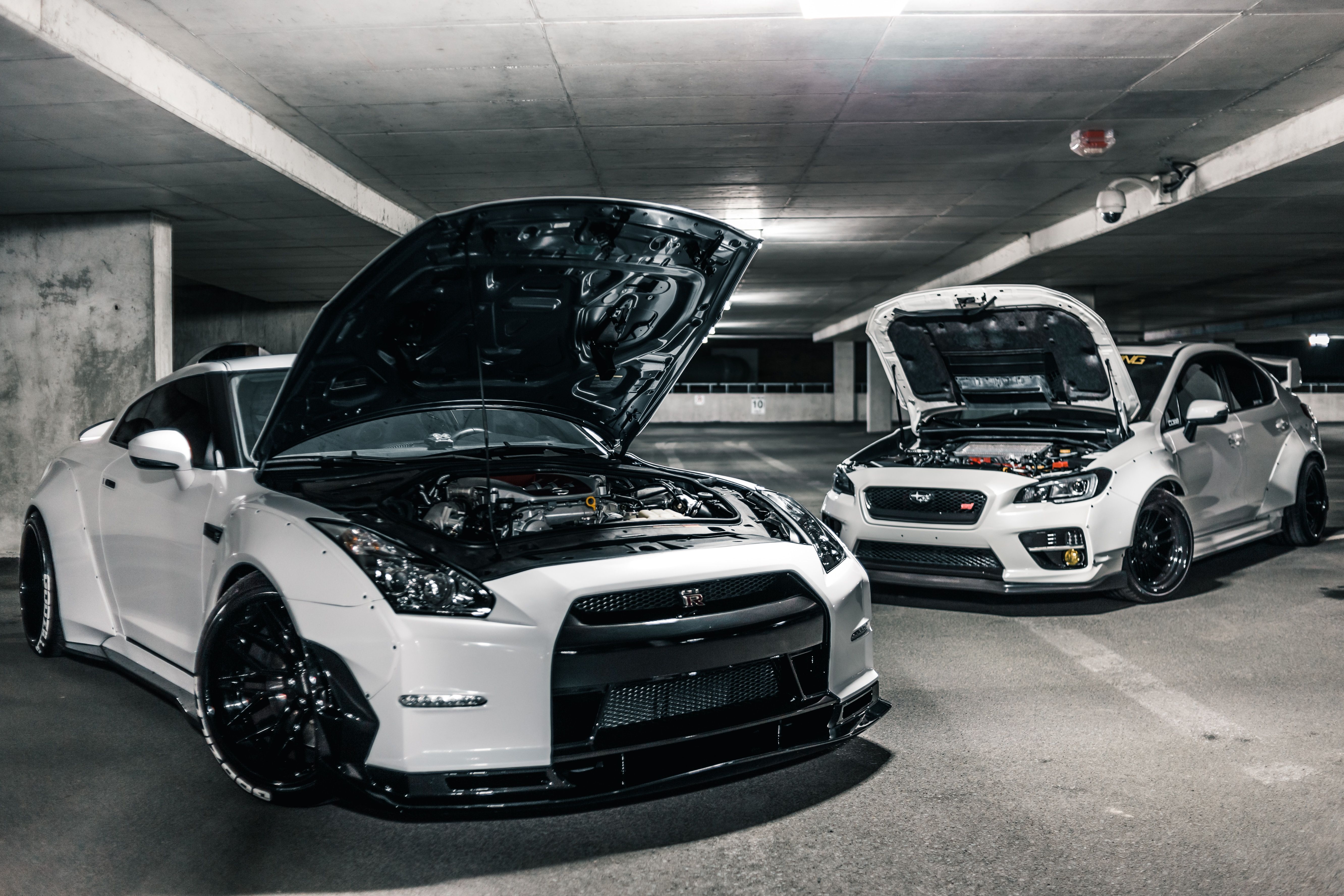 Two white sports cars with their hoods open to show the engine and internals