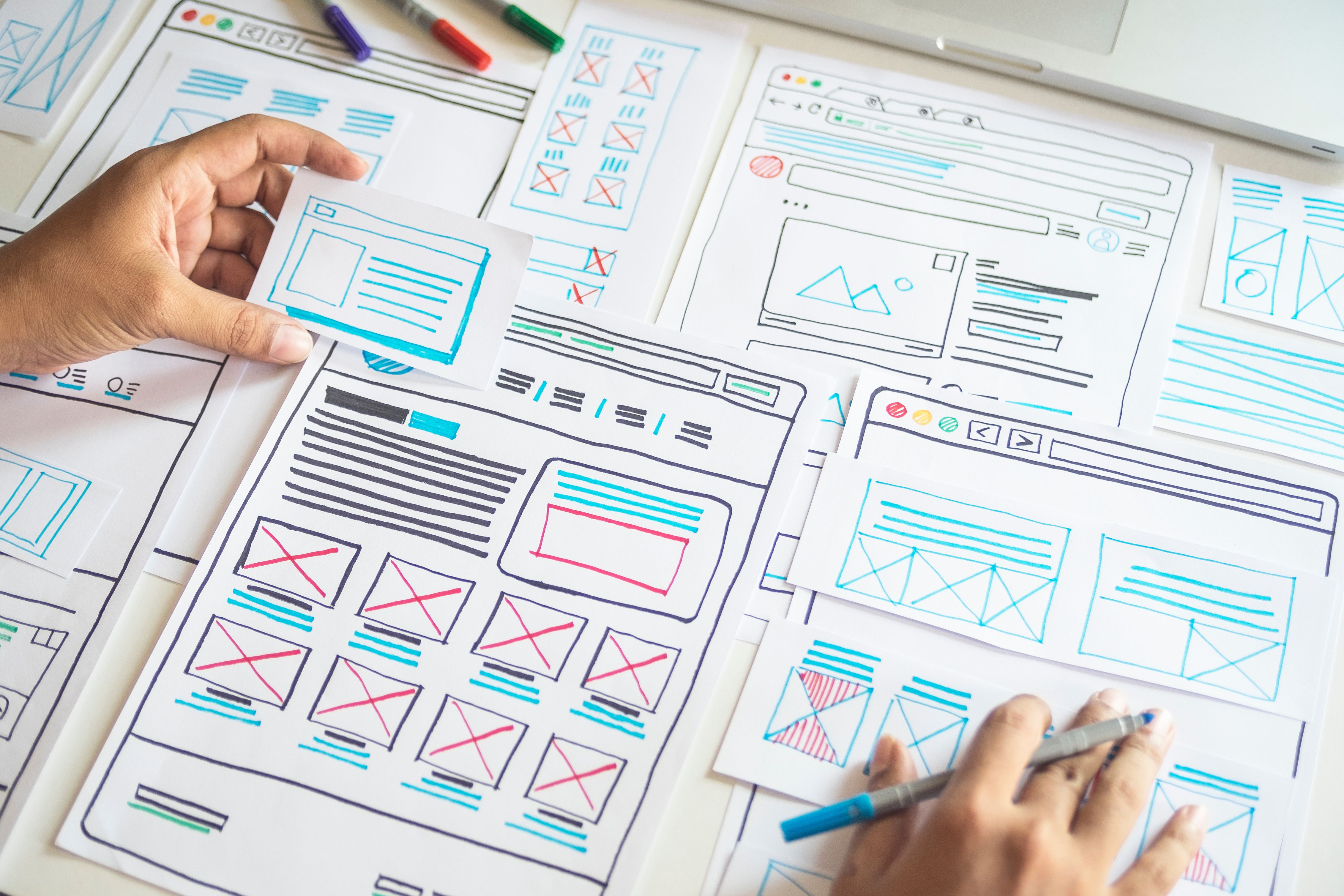 Overhead view of a person assembling a colorful hand-drawn wireframe on a desk