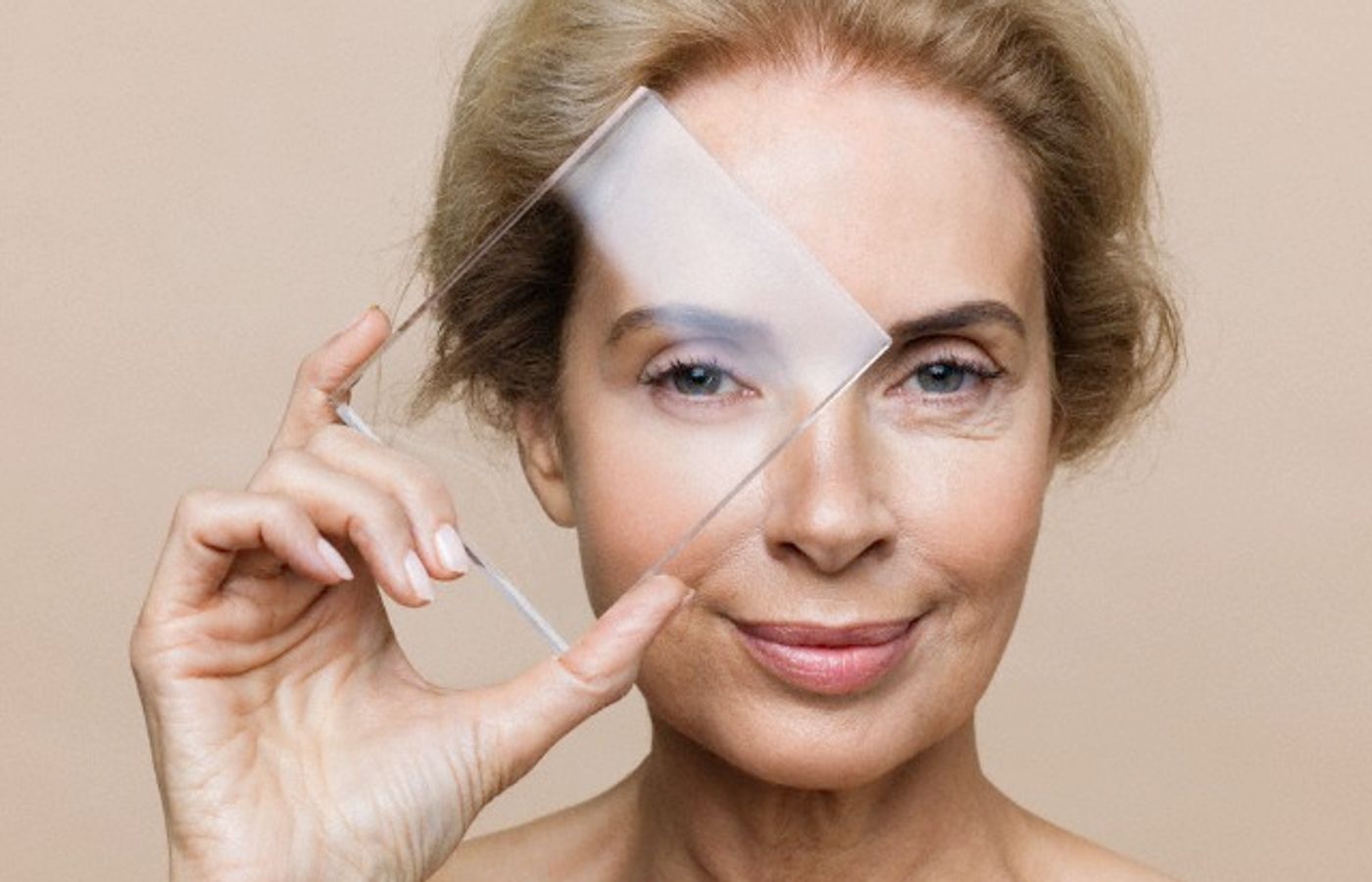 Studio shot of smiling middle-aged woman with younger skin viewed through glass