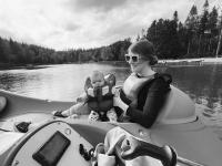 A baby in a lifejacket sits on her mothers lap. They are on a pedalo in the middle of a lake surrounded by trees, which are in the background.