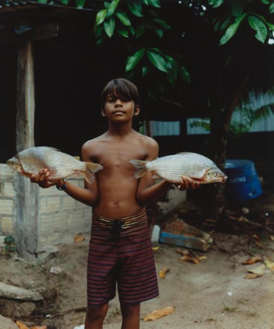 a shirtless boy is holding two fish in his hands