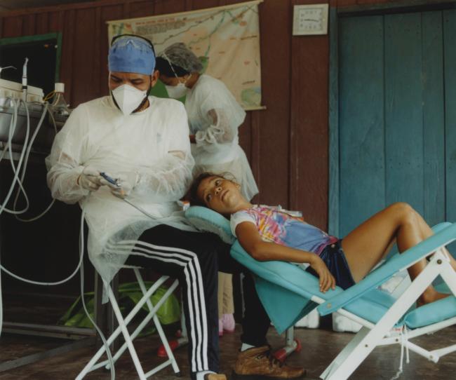 a dentist is working on a young girl 's teeth in a dental chair .