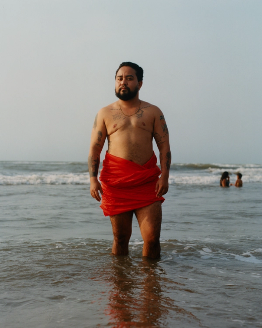 a shirtless man in a red skirt stands in the ocean