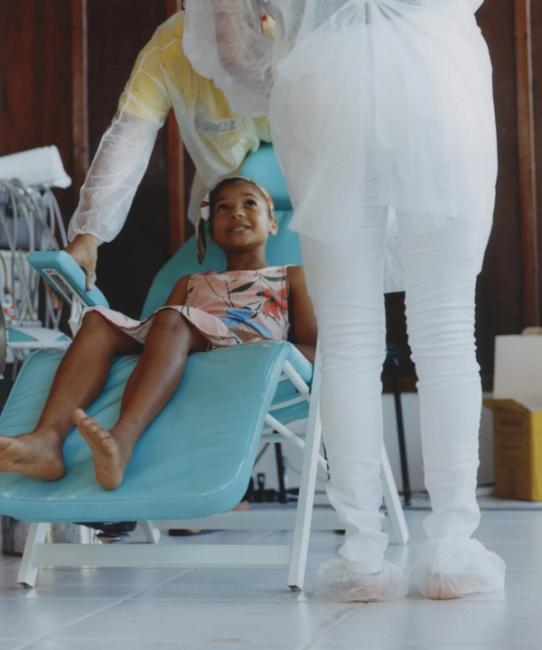 a little girl is sitting in a dental chair with a nurse standing behind her