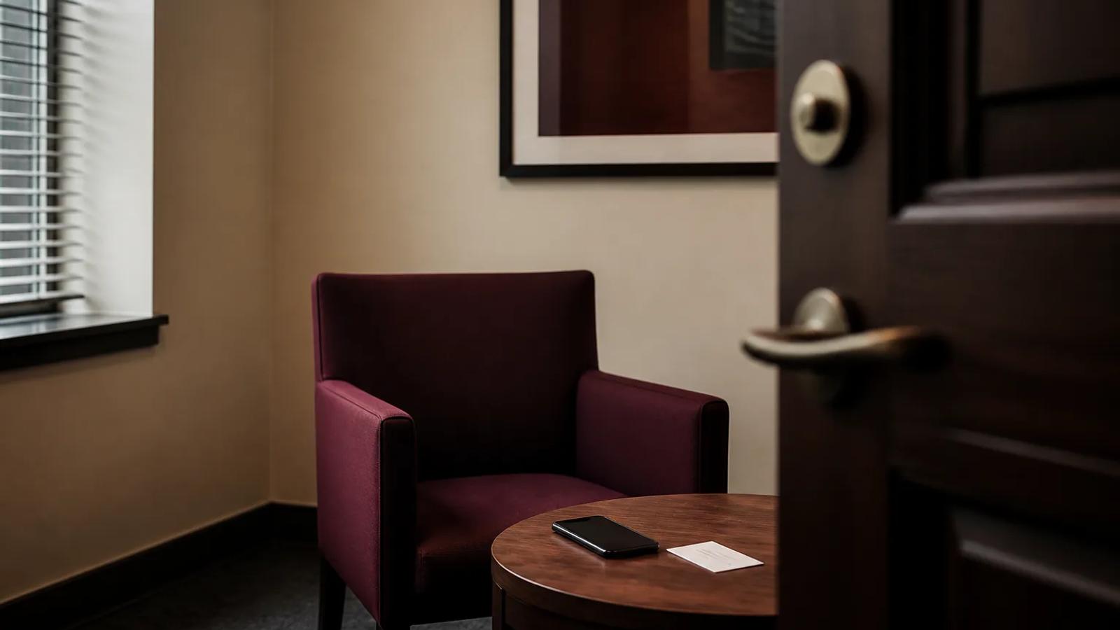An unanswered phone beside a blank interview-room chair and an anonymous investigator card