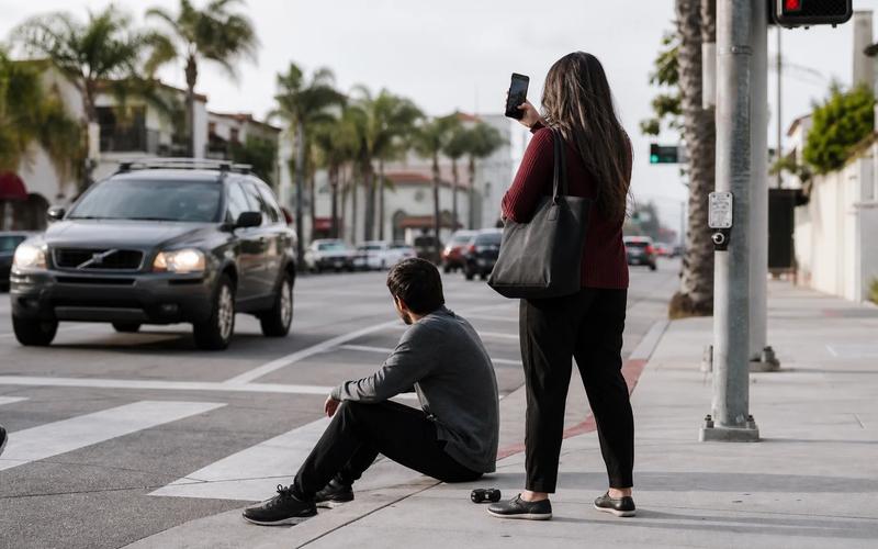 A companion helping a pedestrian at a crosswalk while another person safely photographs the intersection