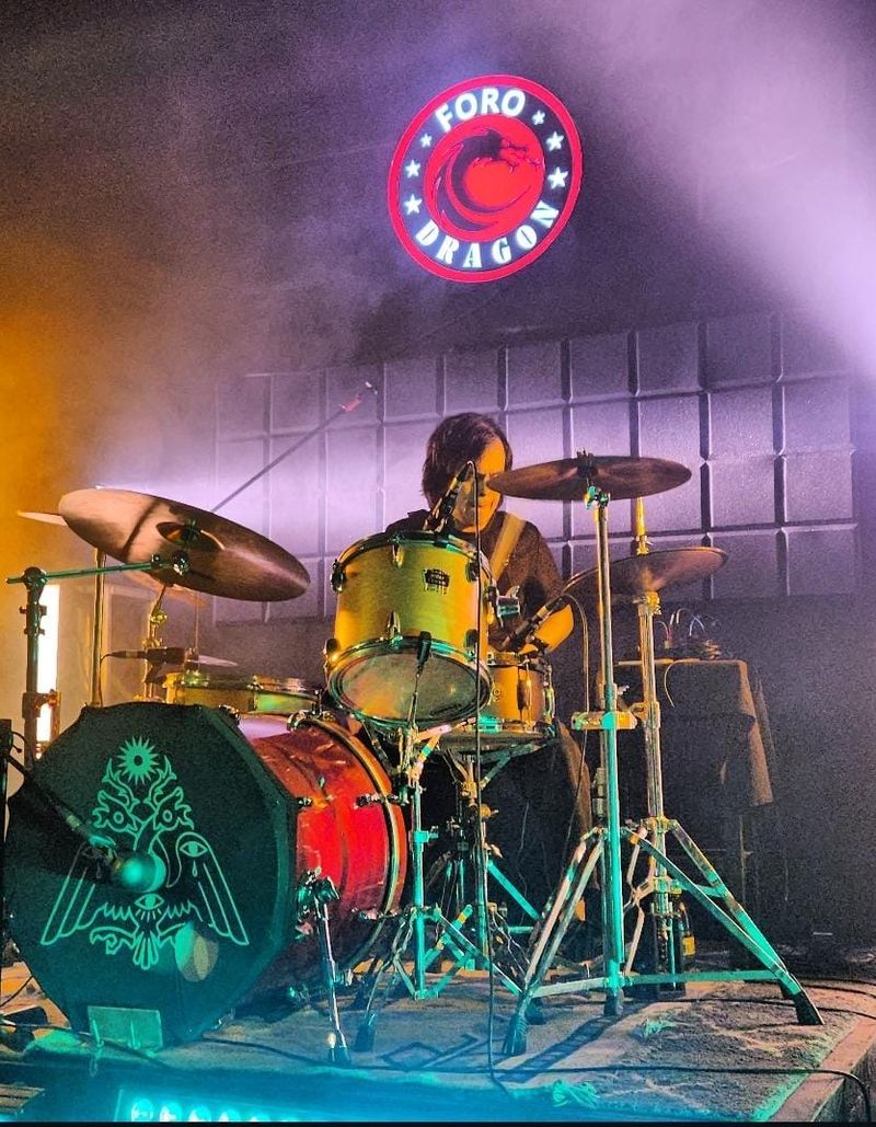 Alex tocando la batería en el escenario con luces de colores y niebla en el fondo