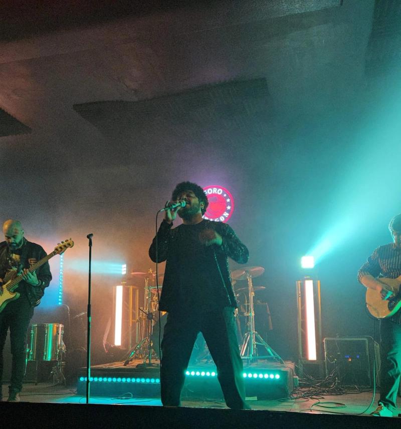 Moisés cantando con un micrófono en un escenario con luces brillantes y coloridas en el fondo