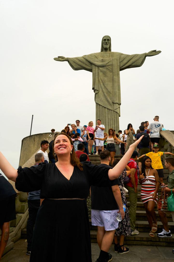 woman standing with her arms outstretched in front of christ the redeemer statue in rio de janeiro, brazil