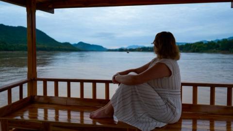 woman sitting on a boat at dusk watching the mekong river in luang prabang, laos