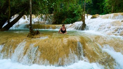 woman sitting in the waterfalls outside luang prabang, laos