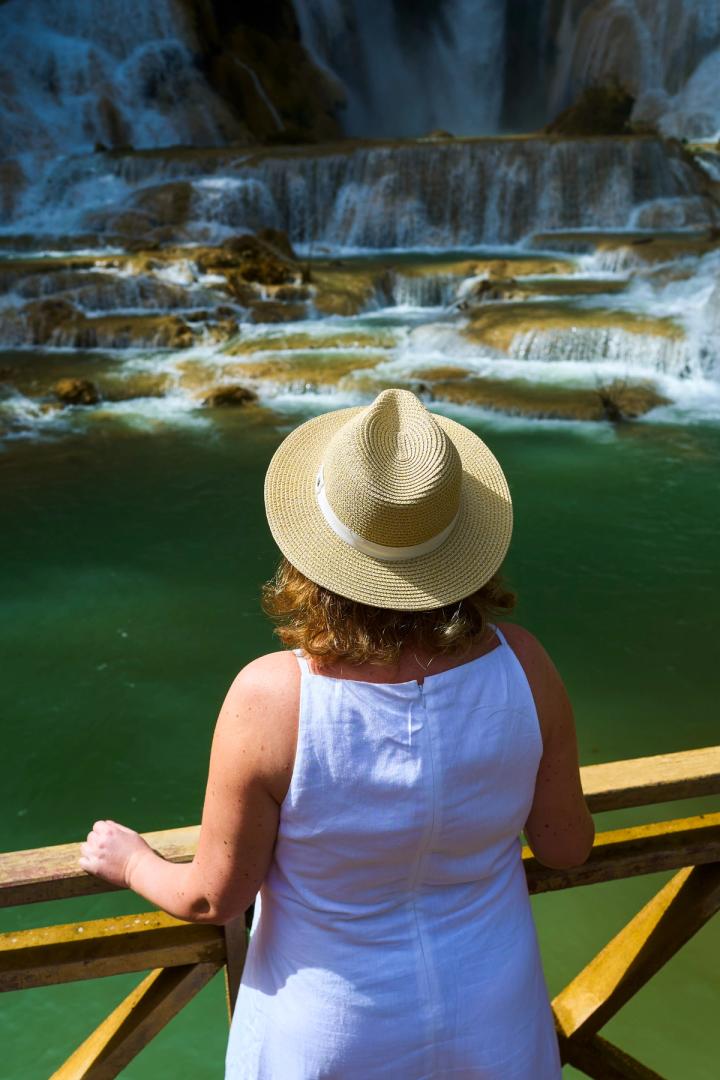 a woman with a hat standing in front of the kung si waterfalls in luang prabang, laos