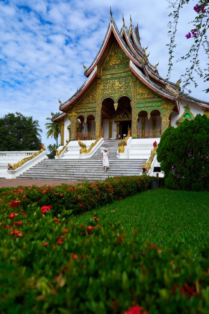 a woman in a white dress walking up the stairs to a temple in luang prabang, laos