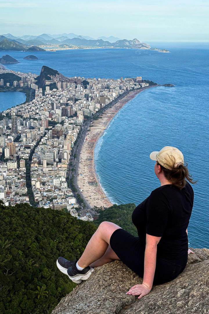 woman sitting at the edge or dois irmaos looking out over rio de janeiro, brazil