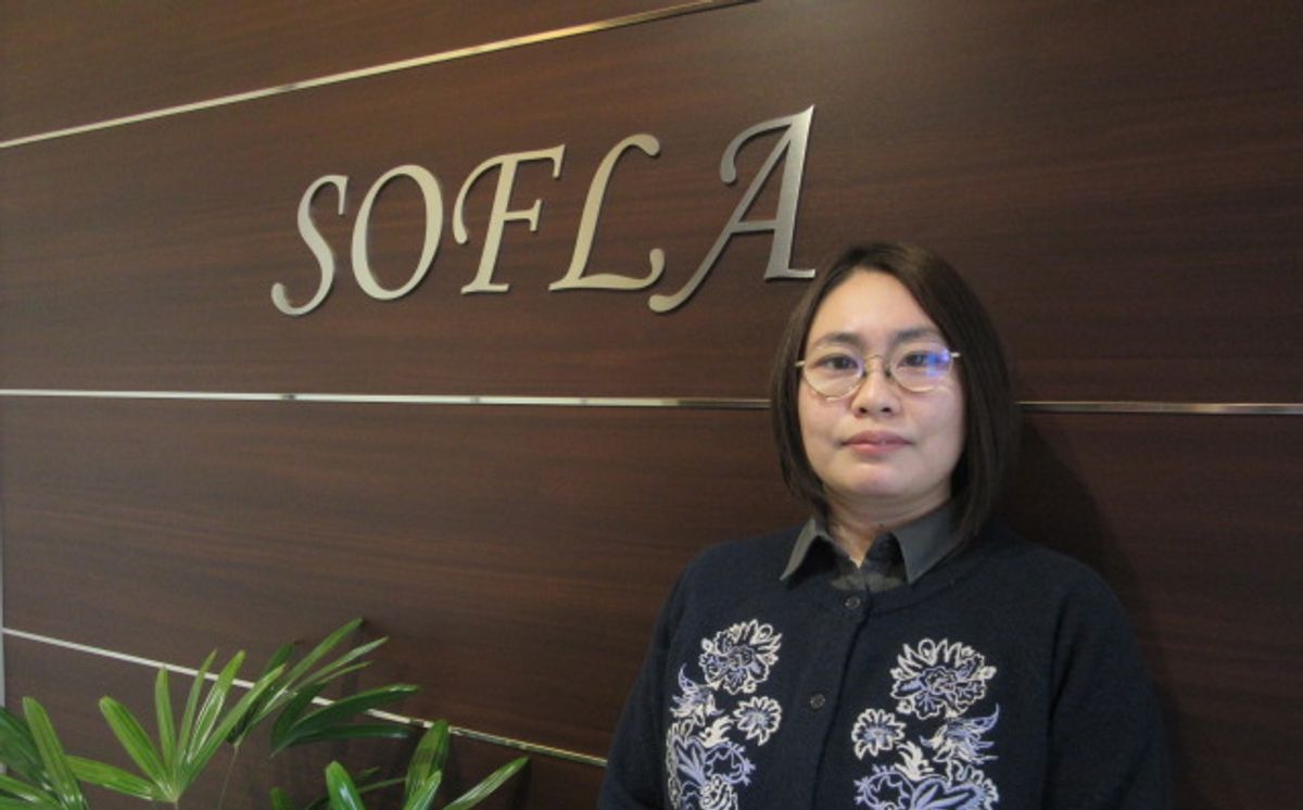 ソフラ株式会社 経営管理部 業務・総務チームの長谷川様（SOFLAのロゴが掲げられたオフィスにて）