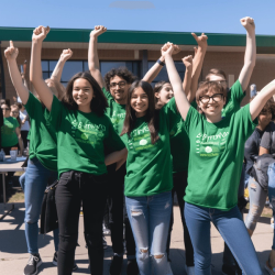 Jugendliche strecken die Arme in Gewinnerpose in de Höhe vor Schulgebäude