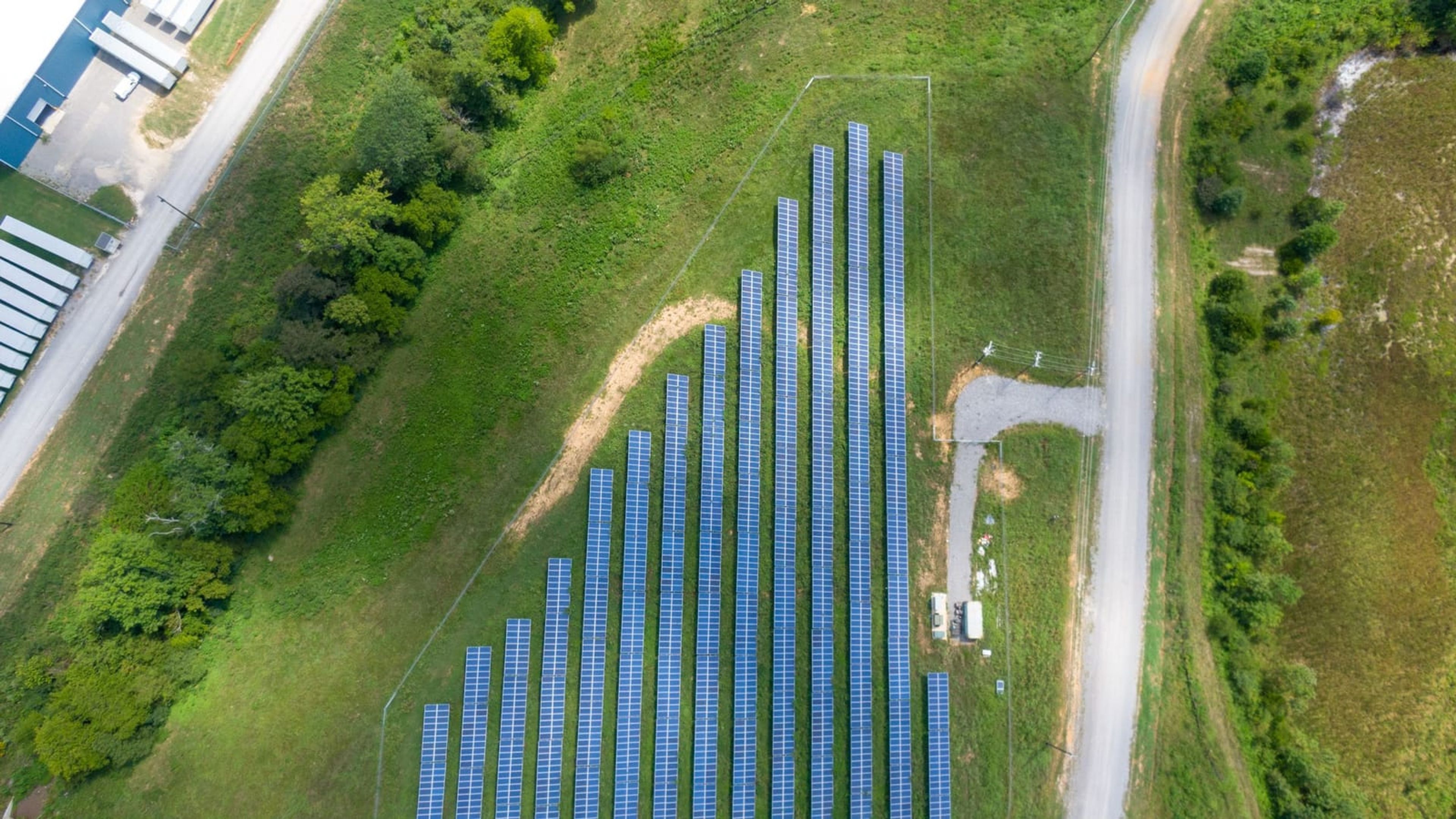 Vista aérea de usina solar ao lado de estrada de terra em área rural.