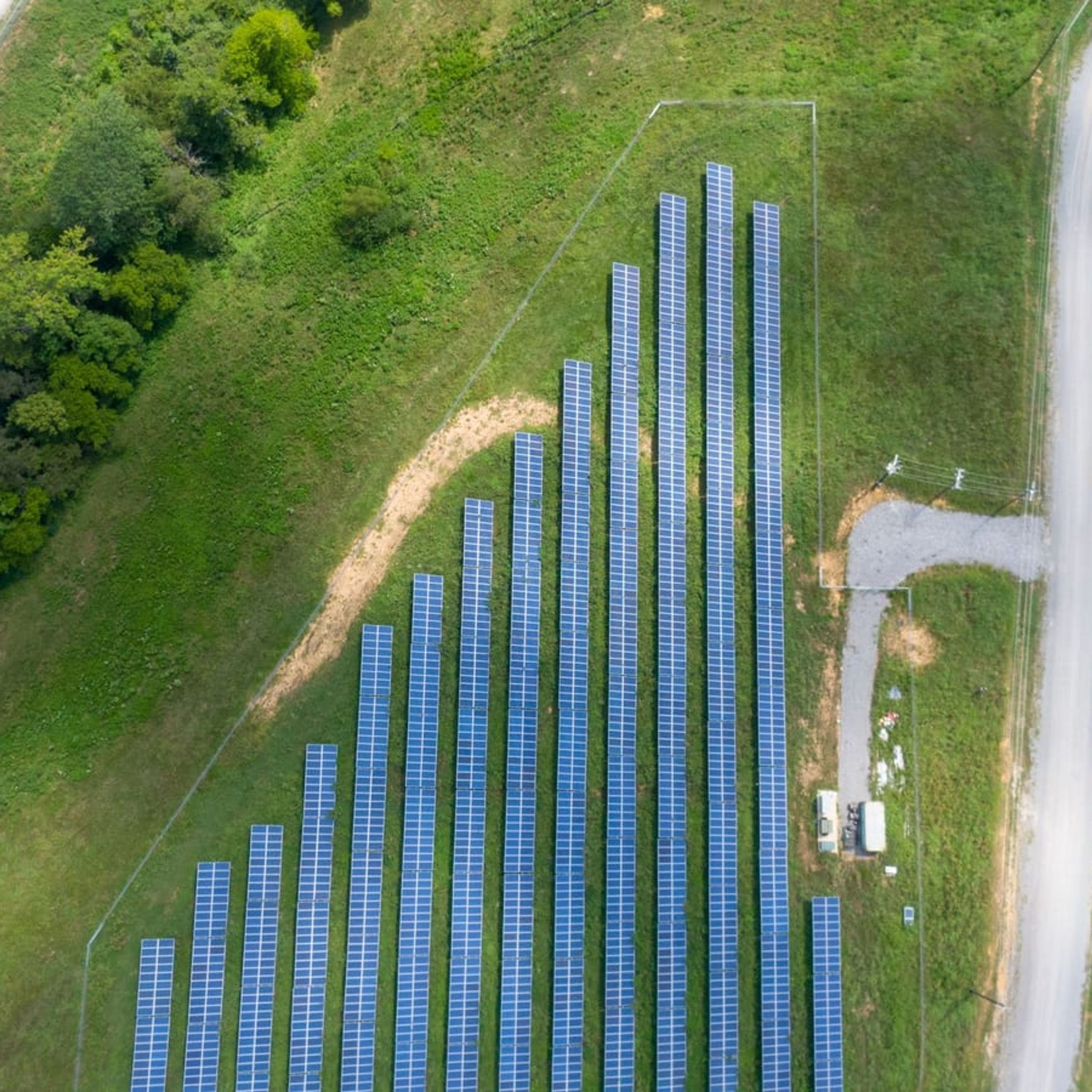 Vista aérea de usina solar ao lado de estrada de terra em área rural.