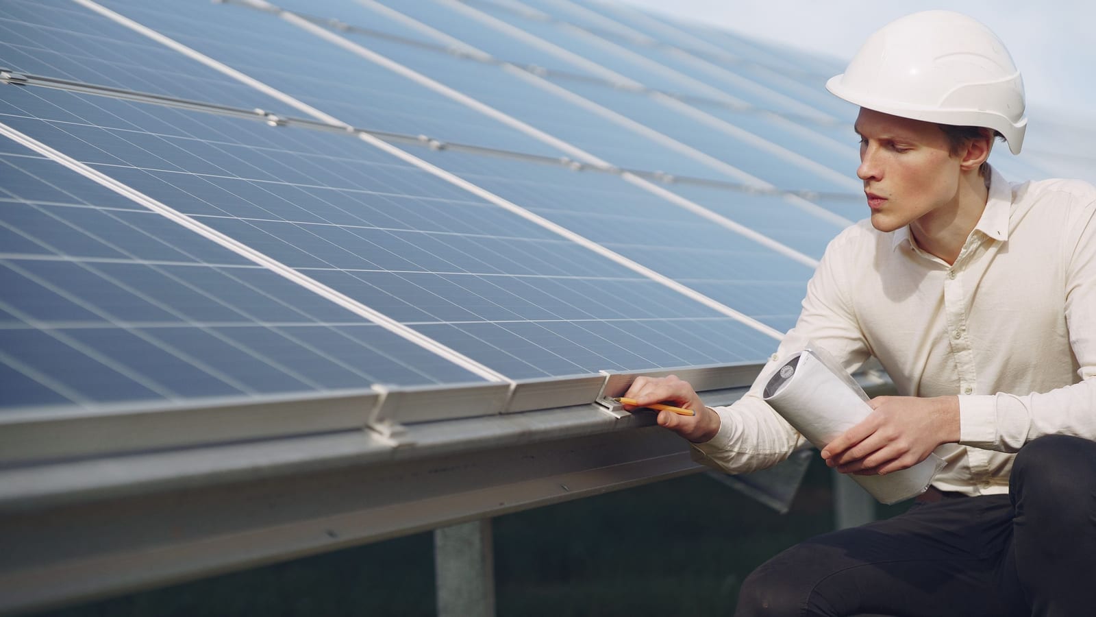 Engenheiro com prancheta inspecionando fileira de módulos fotovoltaicos durante comissionamento.