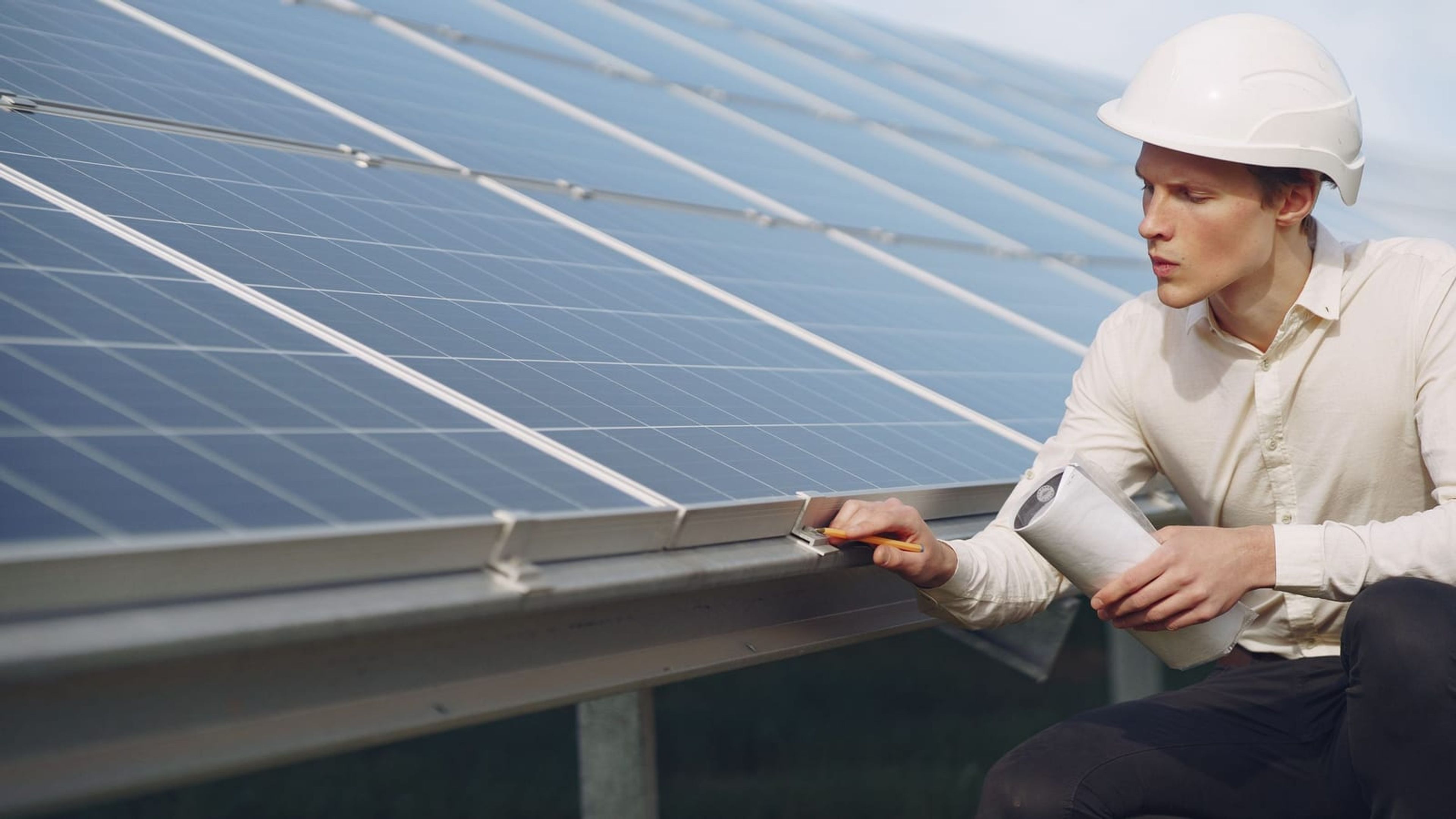 Engenheiro com prancheta inspecionando fileira de módulos fotovoltaicos durante comissionamento.