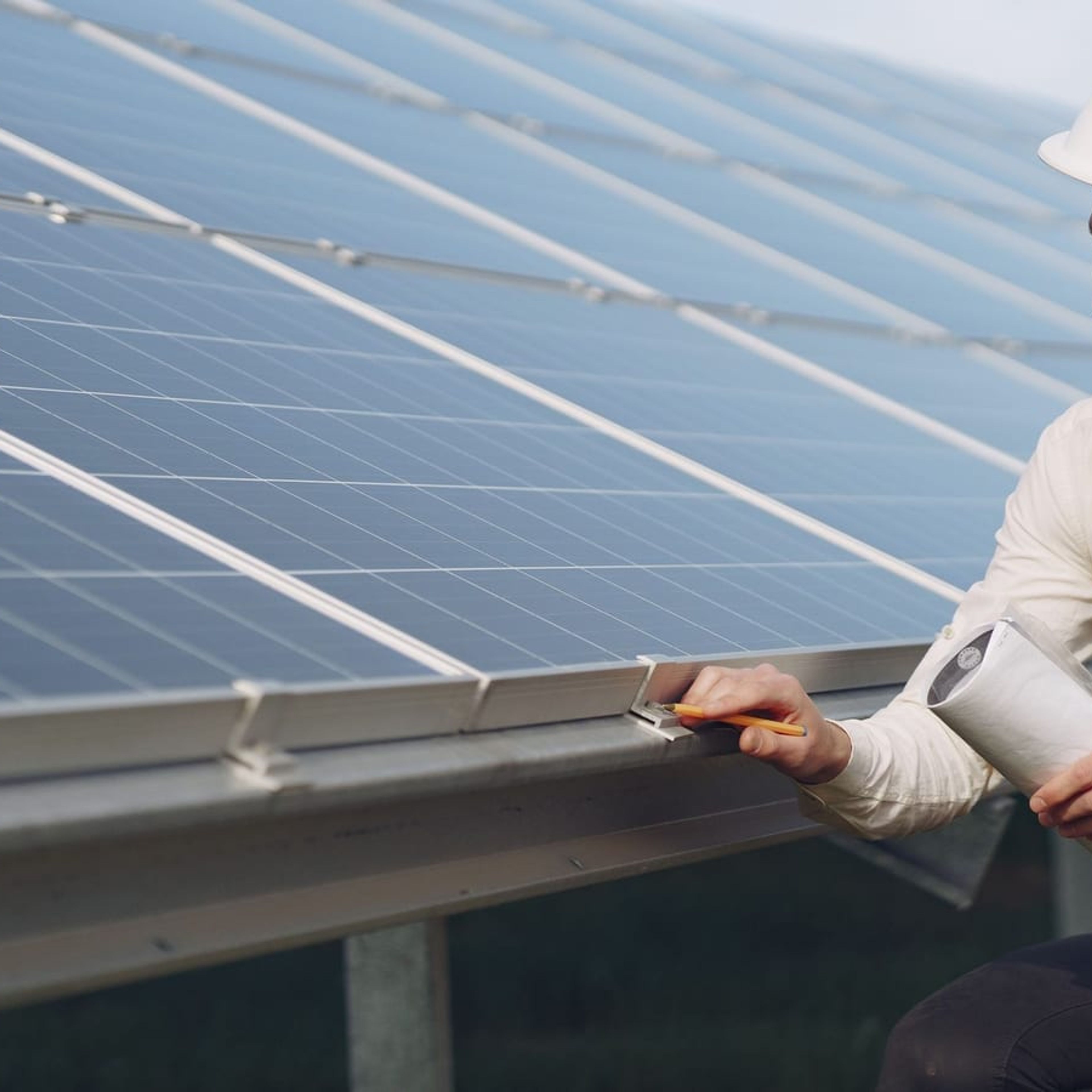Engenheiro com prancheta inspecionando fileira de módulos fotovoltaicos durante comissionamento.