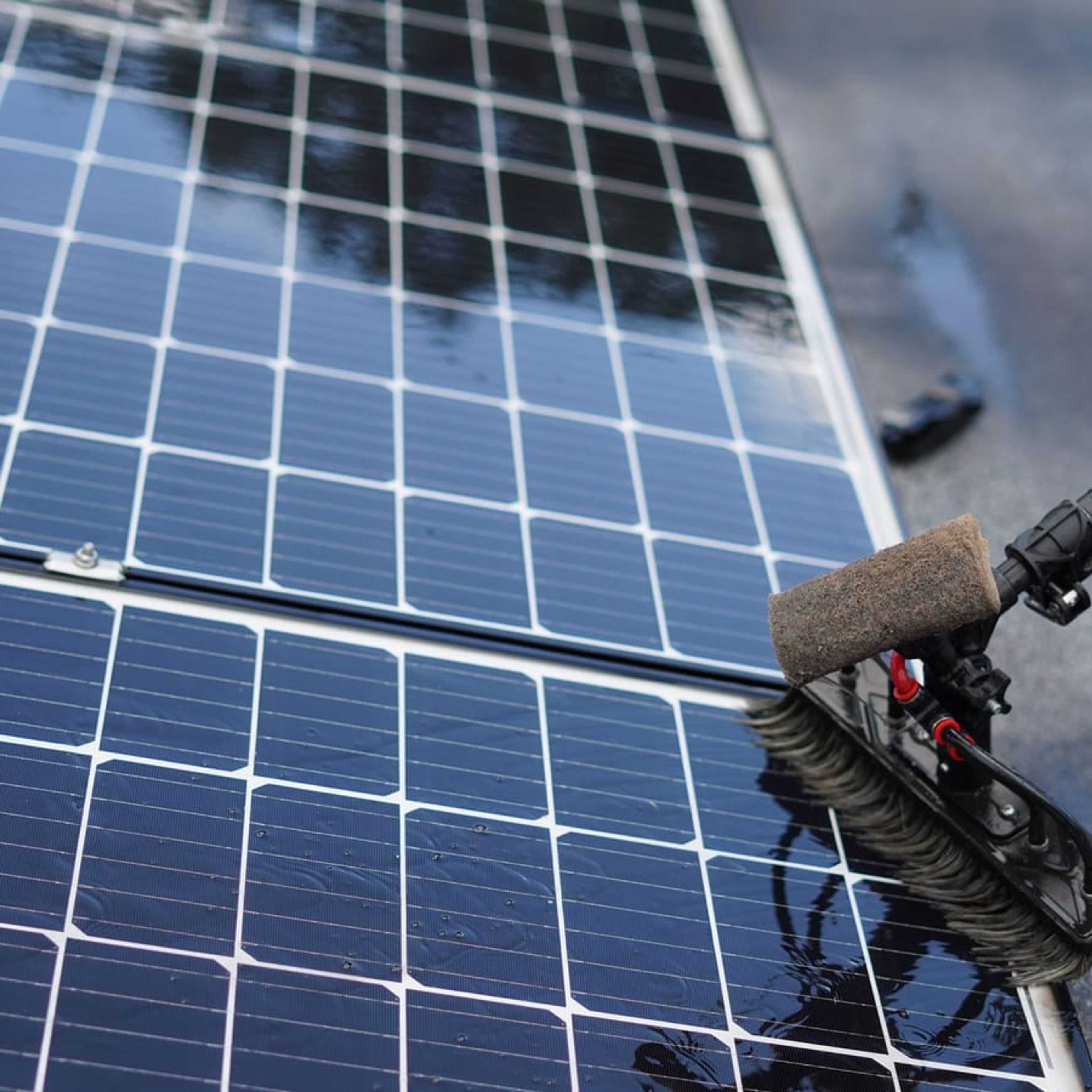 Escova com água limpando a superfície de um módulo fotovoltaico.