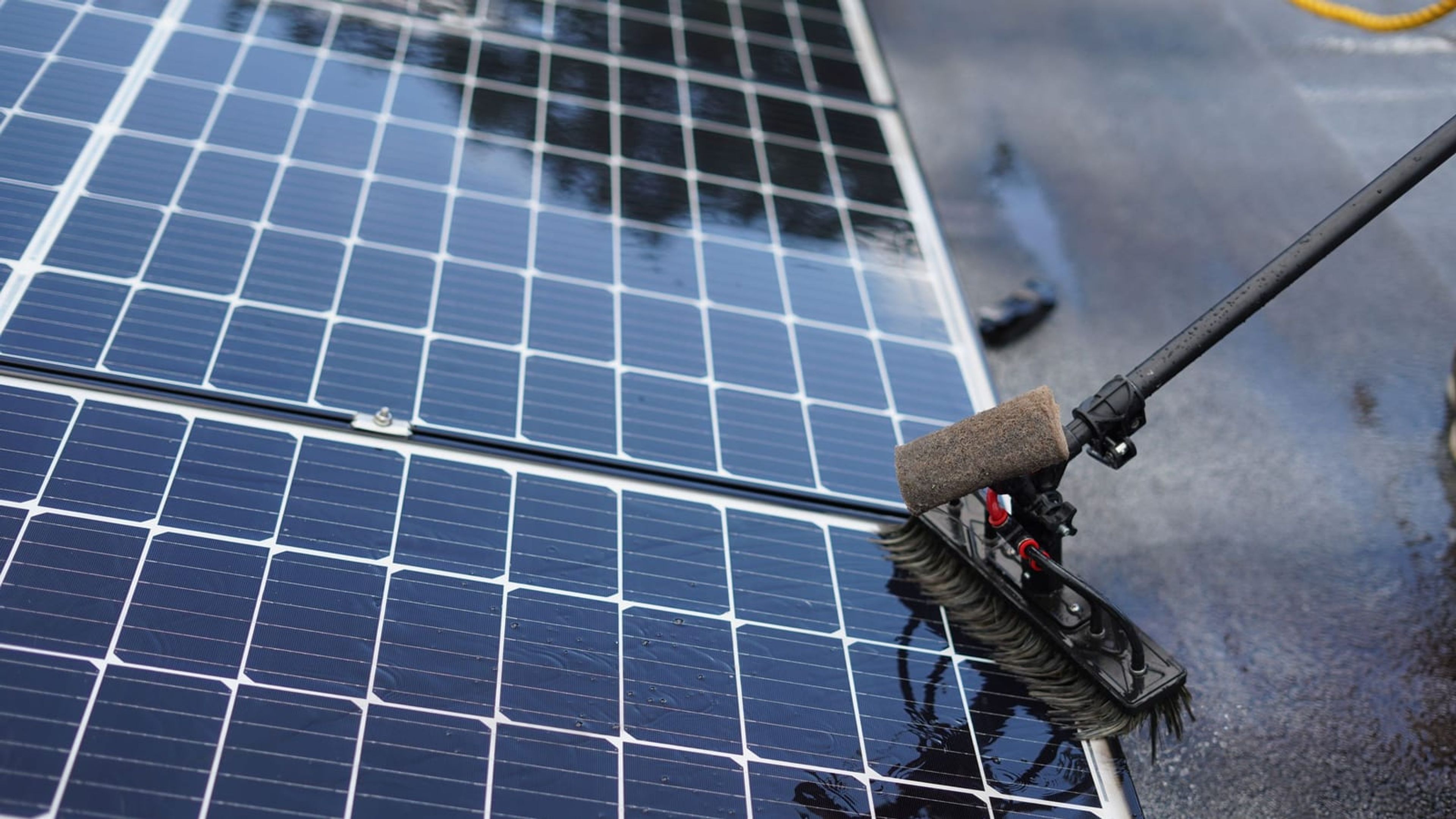 Escova com água limpando a superfície de um módulo fotovoltaico.