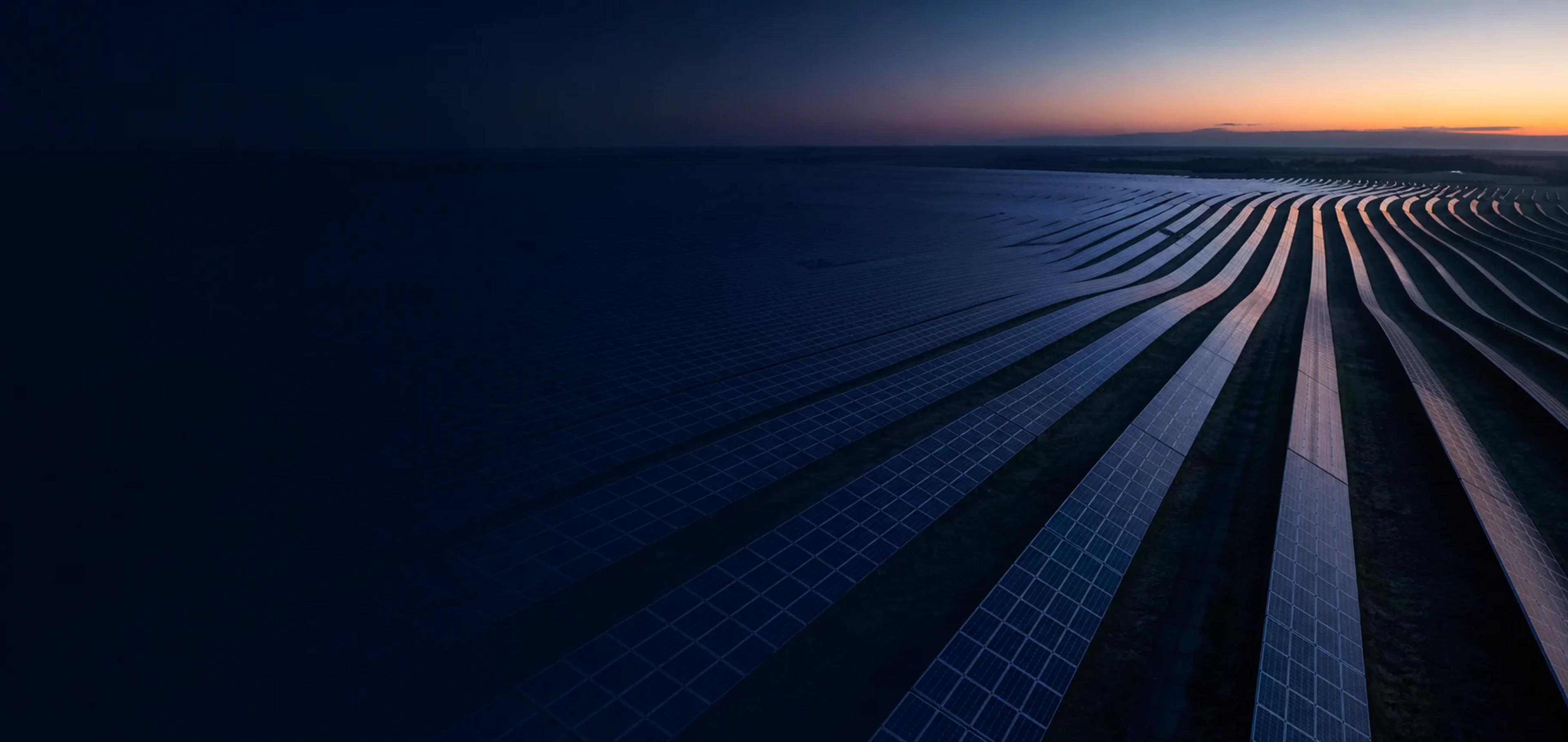 Usina solar de grande porte ao entardecer, com longas fileiras de modulos fotovoltaicos.