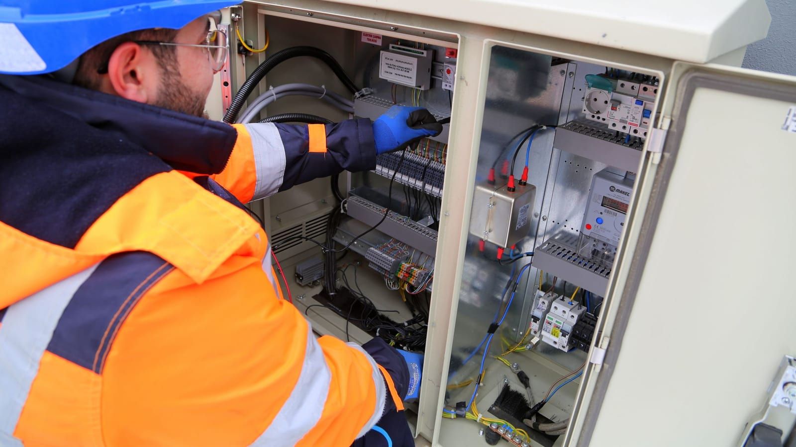 Eletricista trabalhando em quadro de medição e controle com medidor de energia.