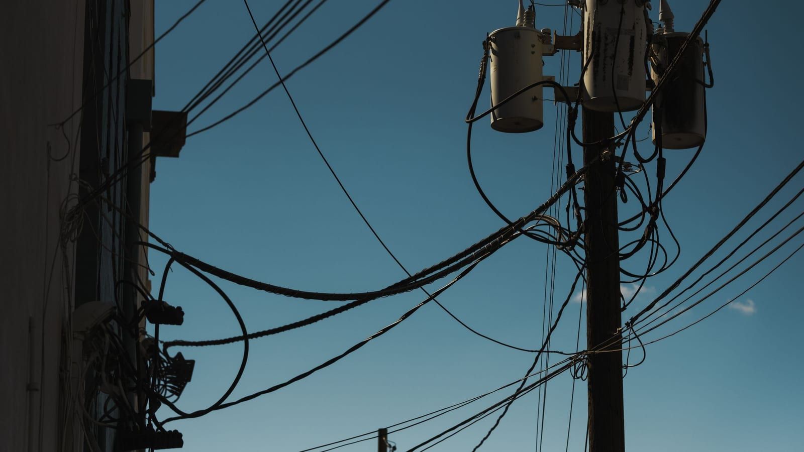 Transformadores de distribuição instalados em poste com cabos da rede elétrica.