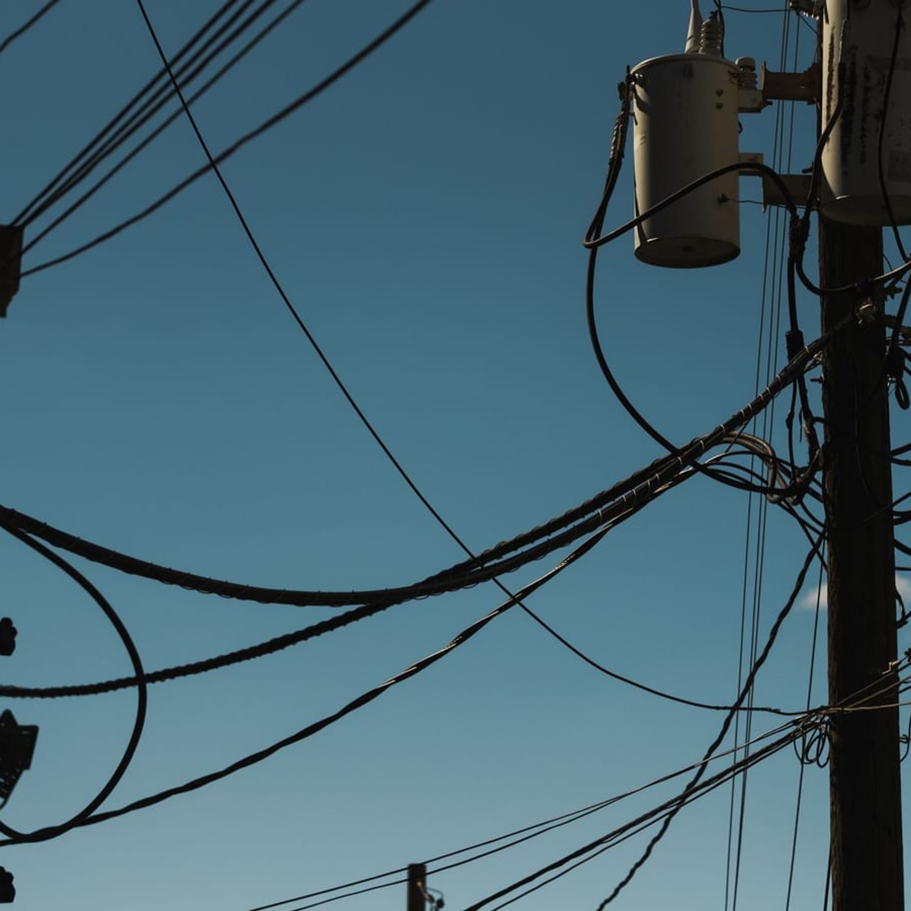 Transformadores de distribuição instalados em poste com cabos da rede elétrica.