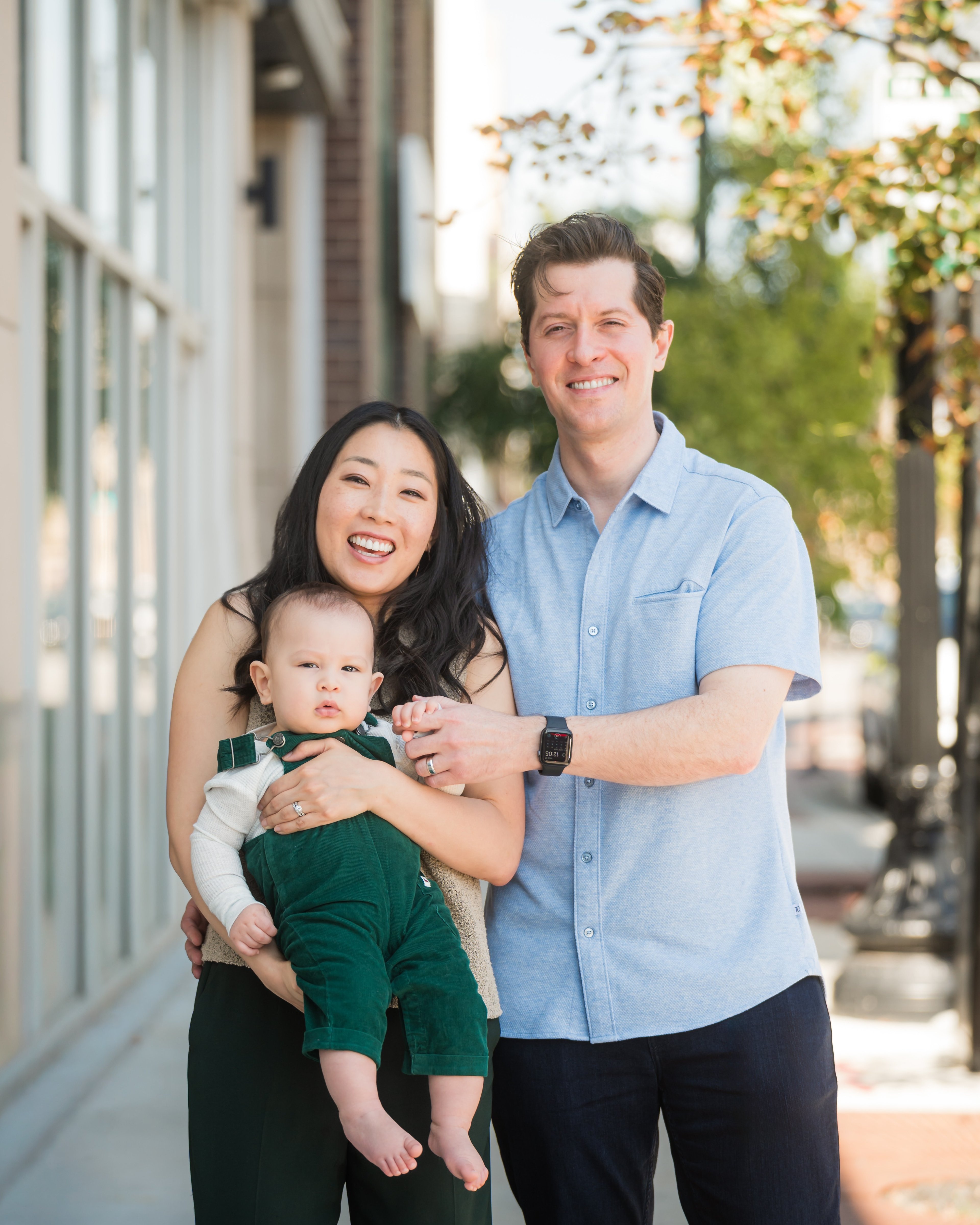 Dr. Erin Cho with her husband Mark and their baby son standing together on a tree-lined street.