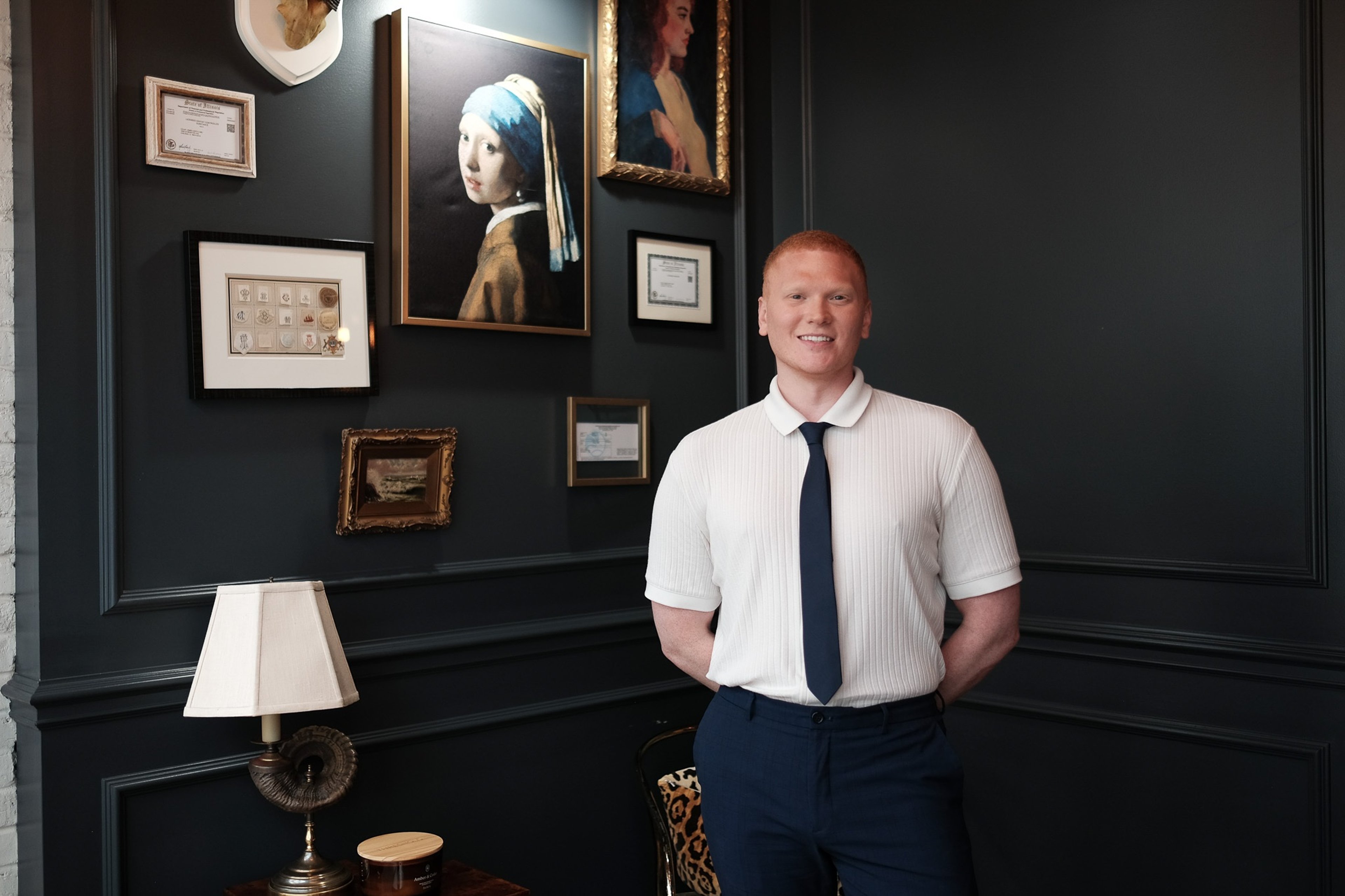 Dr. Colby James Gerth standing in the study-like room at Pearl, in front of a dark wall hung with framed pictures, mounted horns, and the Girl with a Pearl Earring.