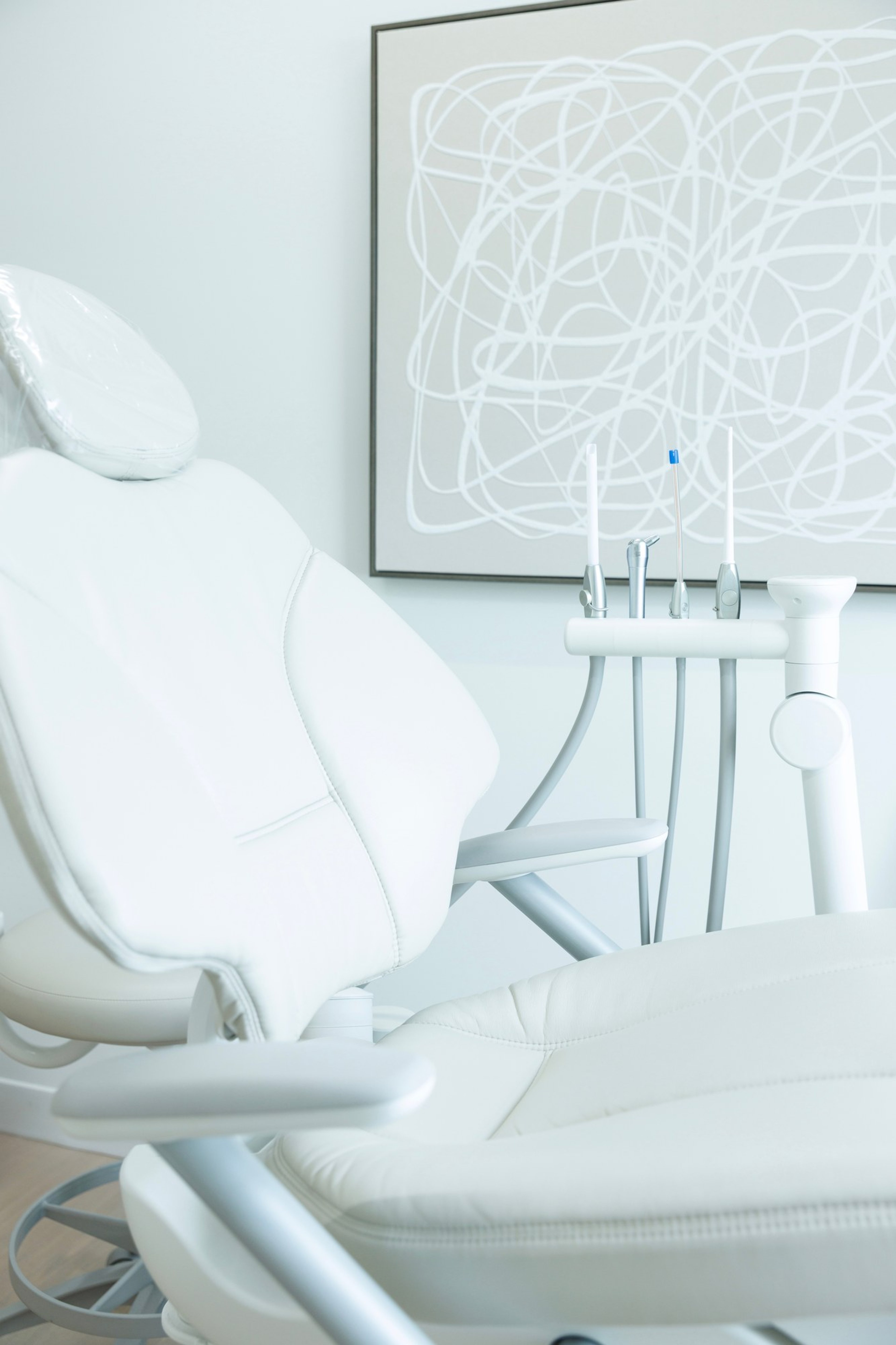 A white dental chair in a bright treatment room at Ever Dental Studio, instruments hanging neatly below a framed abstract line drawing.