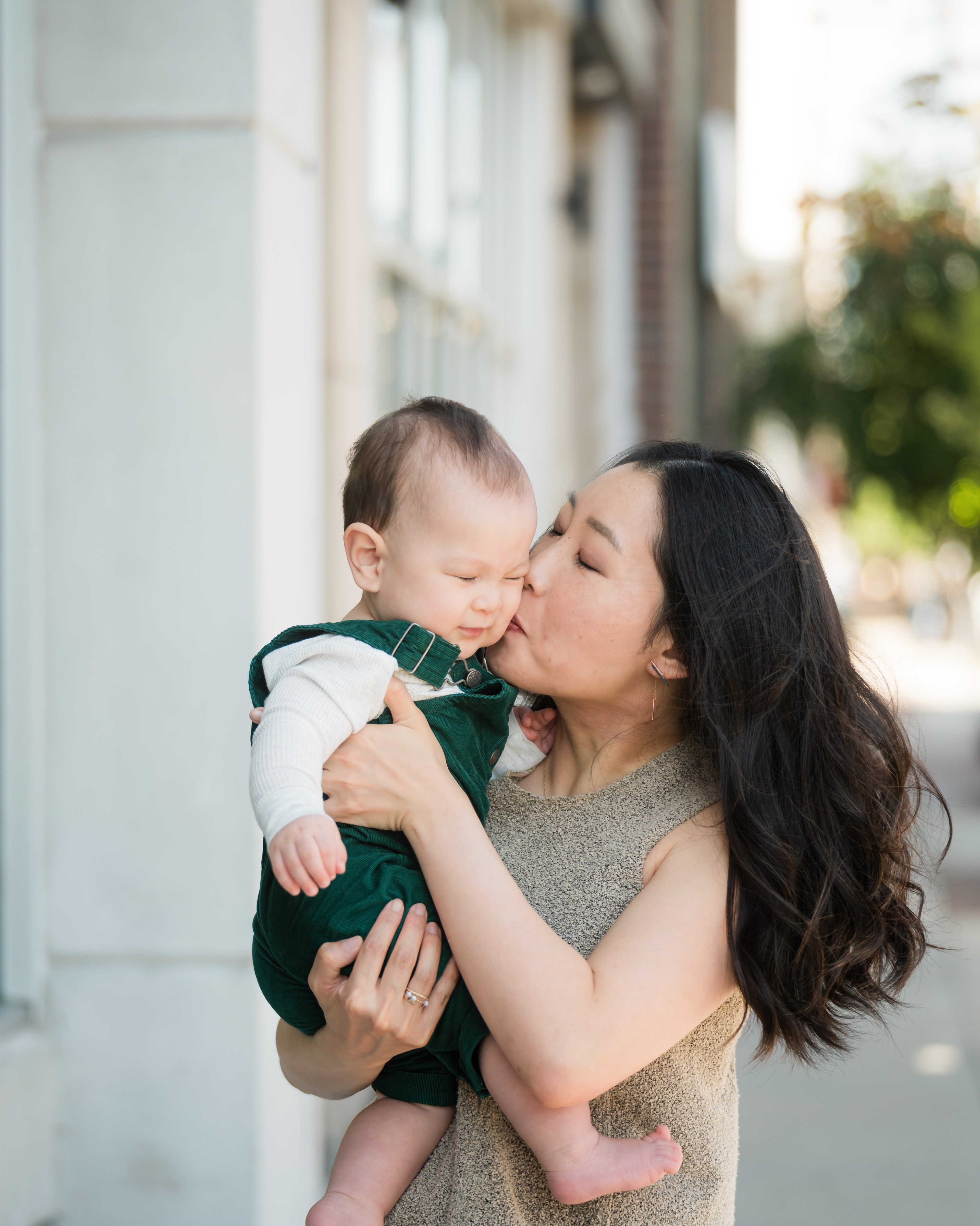Dr. Erin Cho holding her infant son and kissing his head on a city sidewalk.