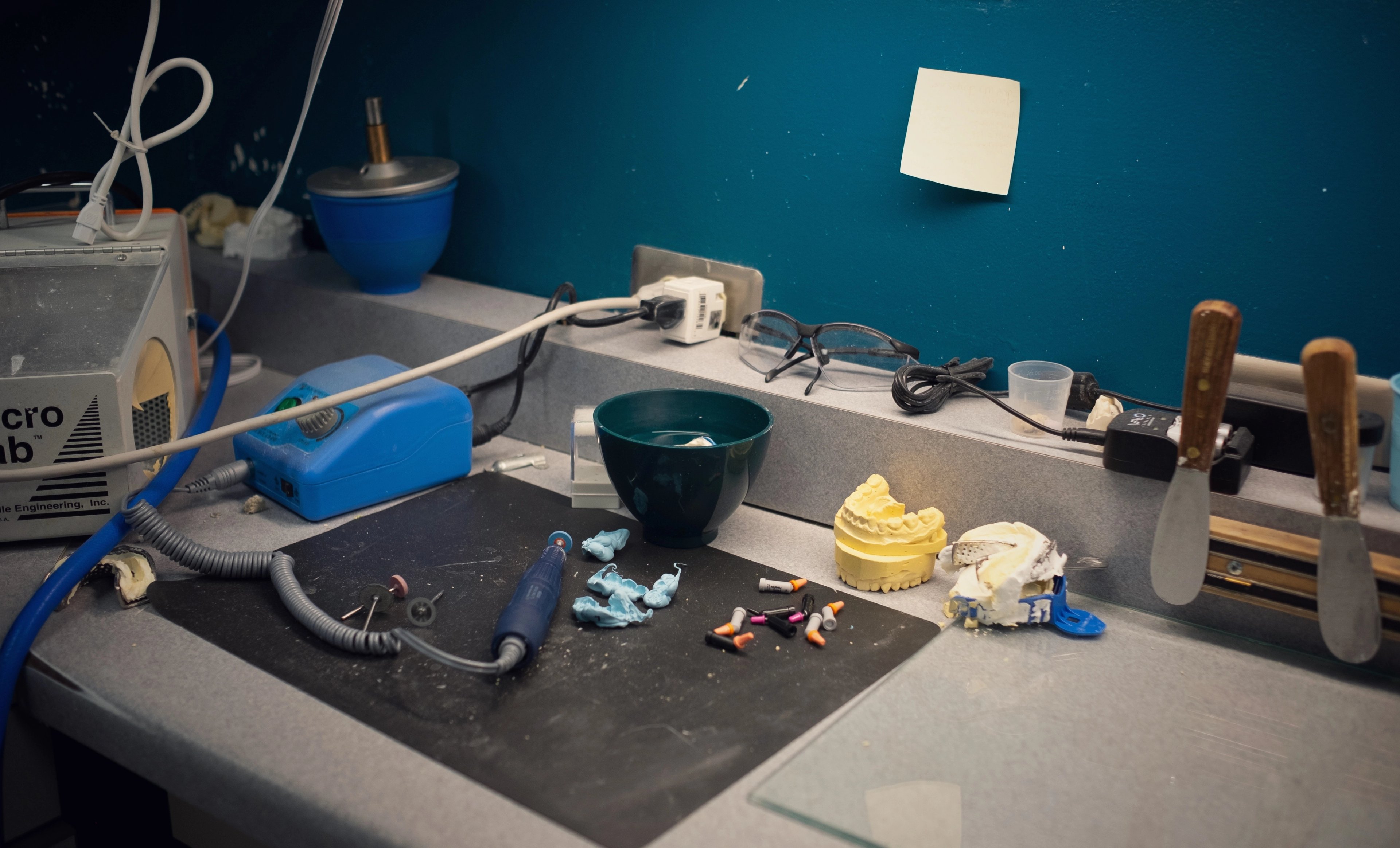 A workstation at the practice with crown materials, instruments, and a sticky note on a teal wall.