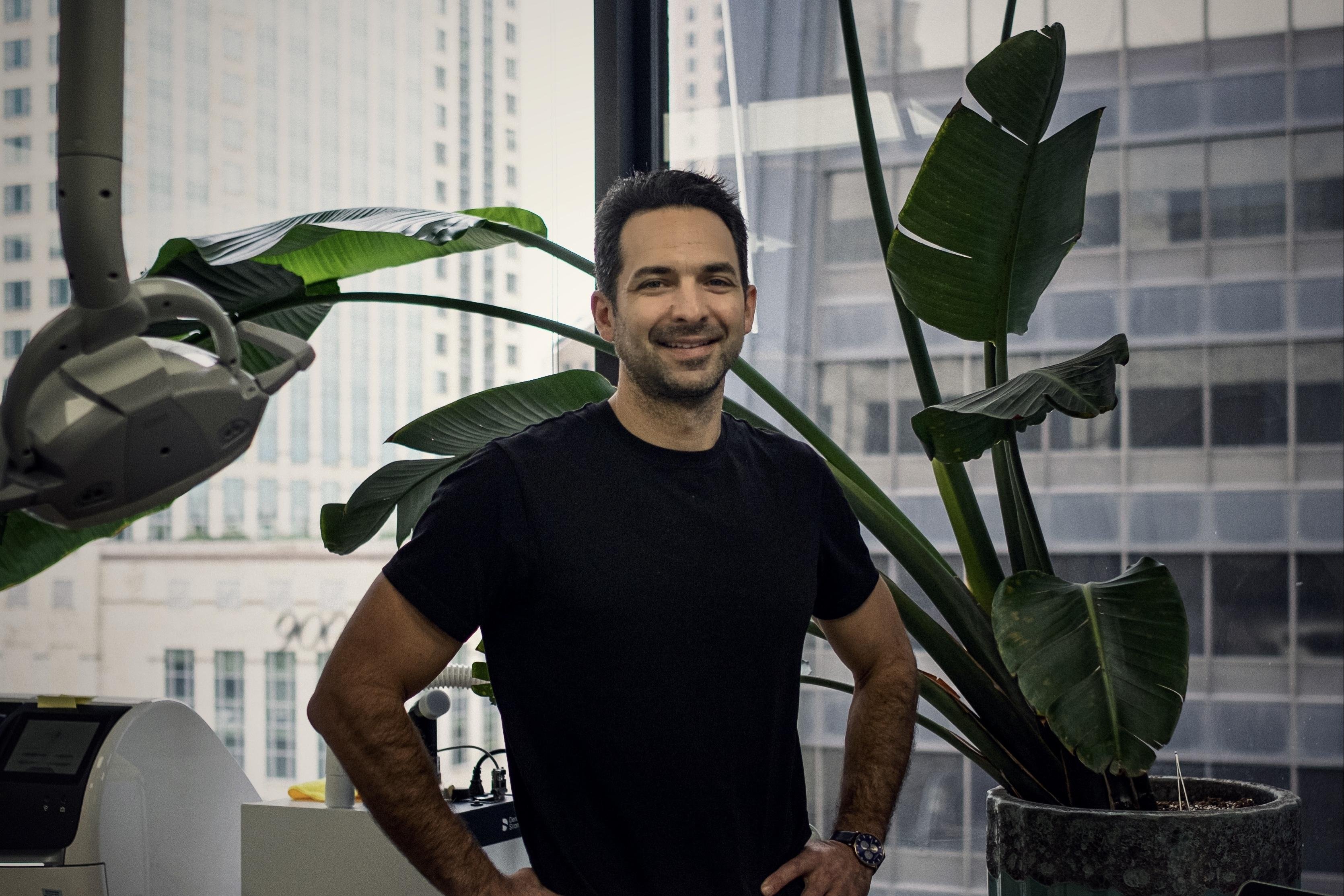 Dr. Louis Santini standing in his downtown Chicago practice, plants beside him, the city visible through the window behind.