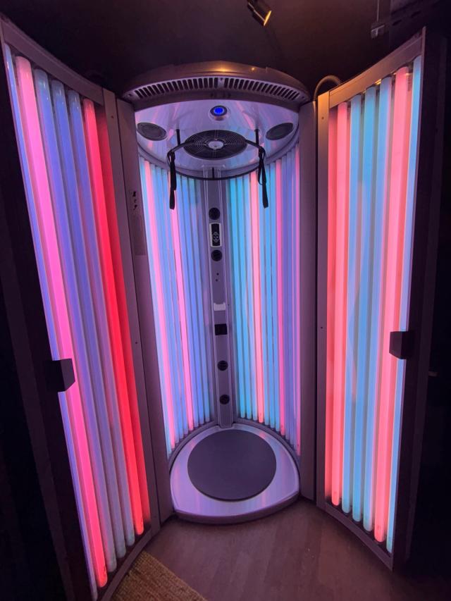 Inside a stand-up sunbed with vertical lamps and an overhead fan