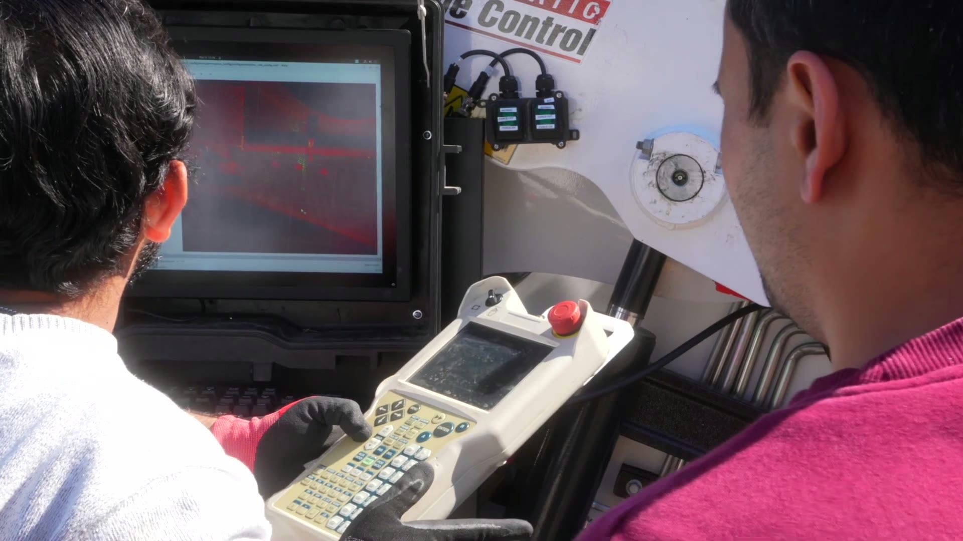 Two Gritt operators on a job site reviewing the system’s red spatial-perception view on a rugged laptop, one holding a handheld controller