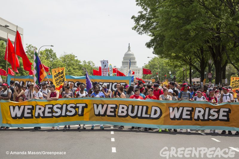 A long line of people hold a banner that says "We resist, we build, we rise" at the 2017 People's Climate March.