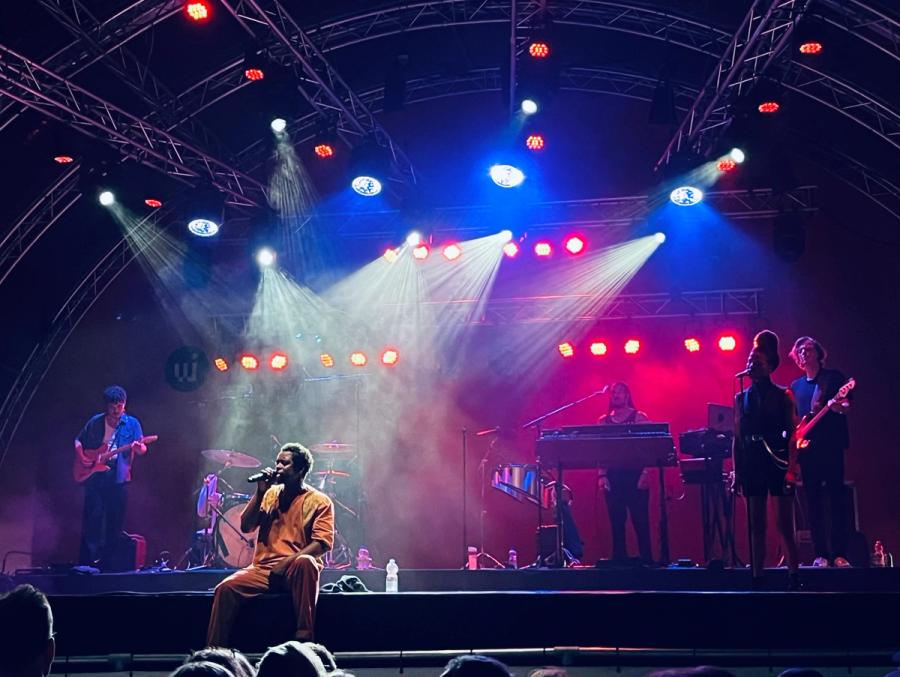 Typhoon seated on the edge of the stage, with next to him his bass player standing, drums behind, and keys, one backing vocal and guitarist on the right