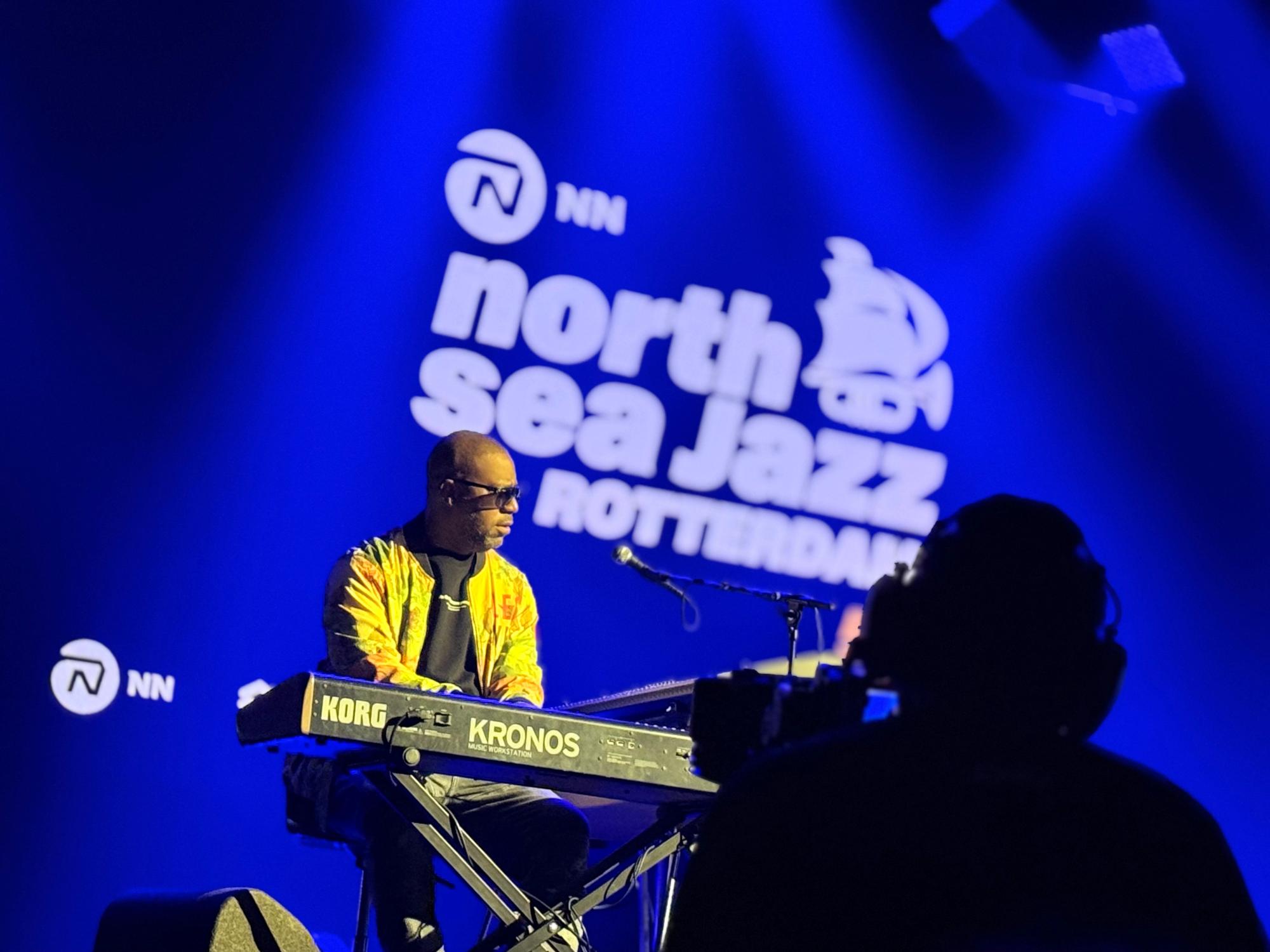 robert glasper playing Korg Kronos keyboard with blue backdrop and blurry north sea jazz logo
