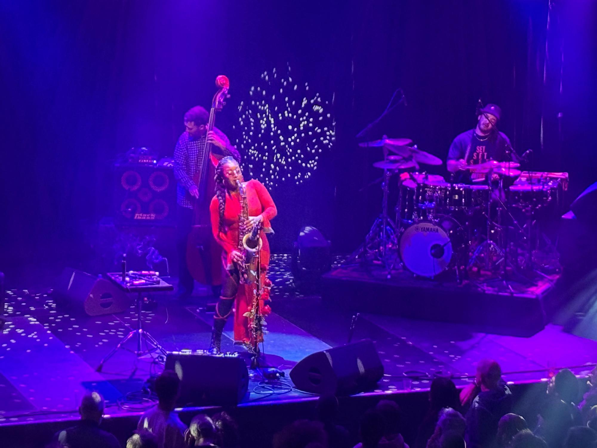 Nubya playing sax, with bass player behind on left and her drummer on right