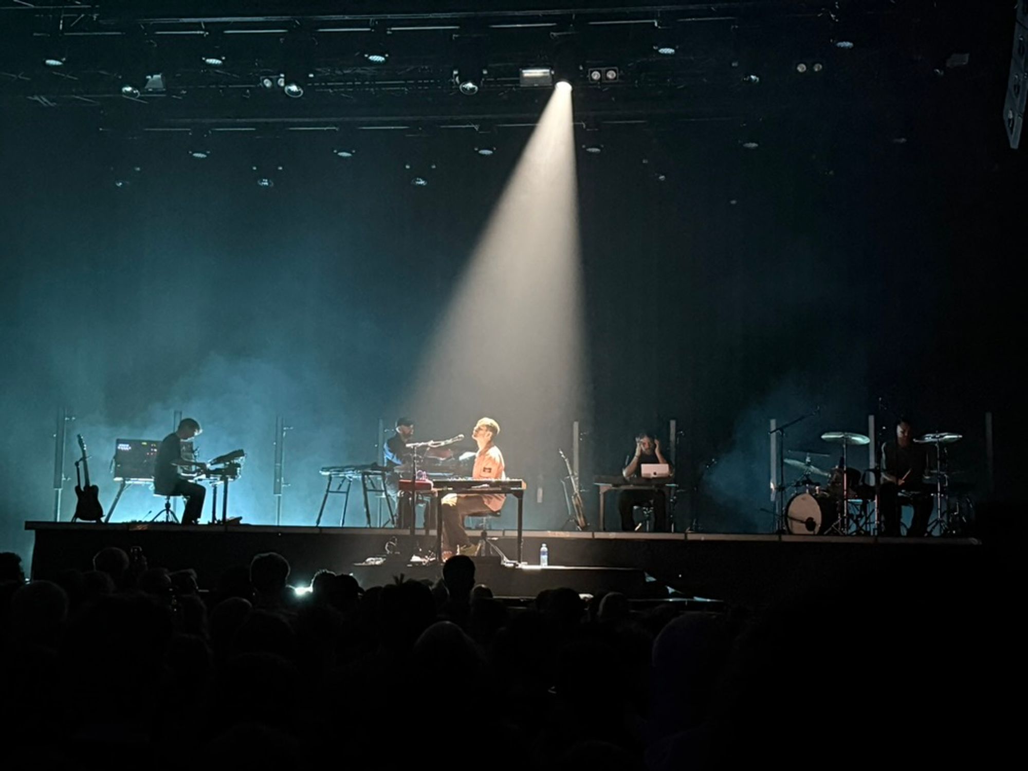 james behind keys with spotlight on him and band behind visible