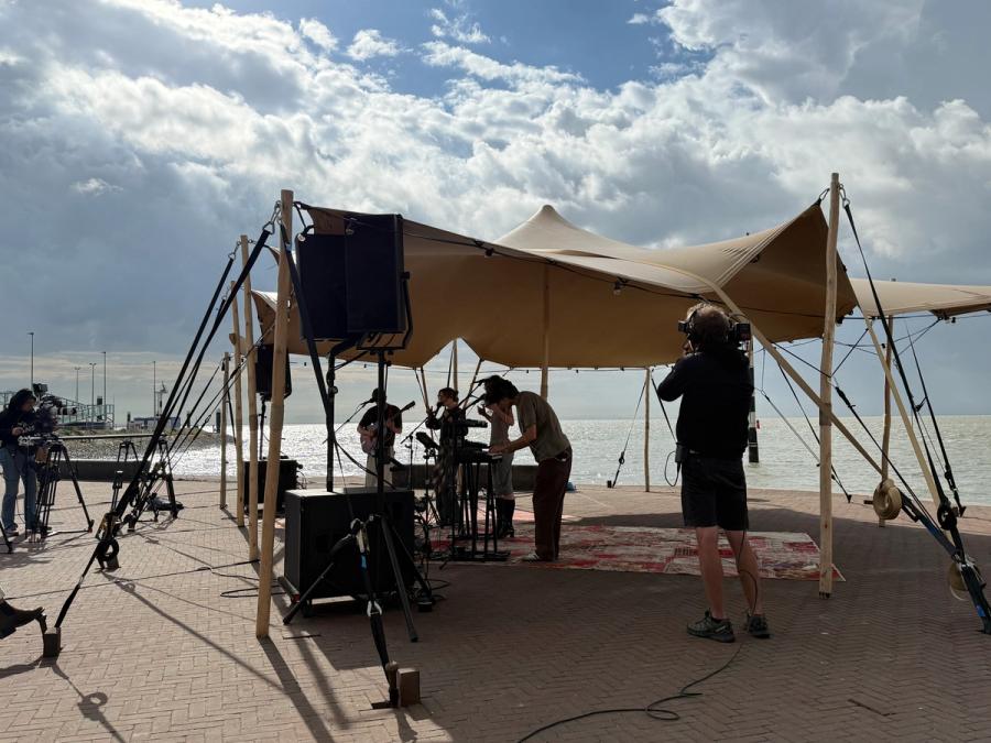band playing under a tent, with the sea right behind and a camera man filming from close up