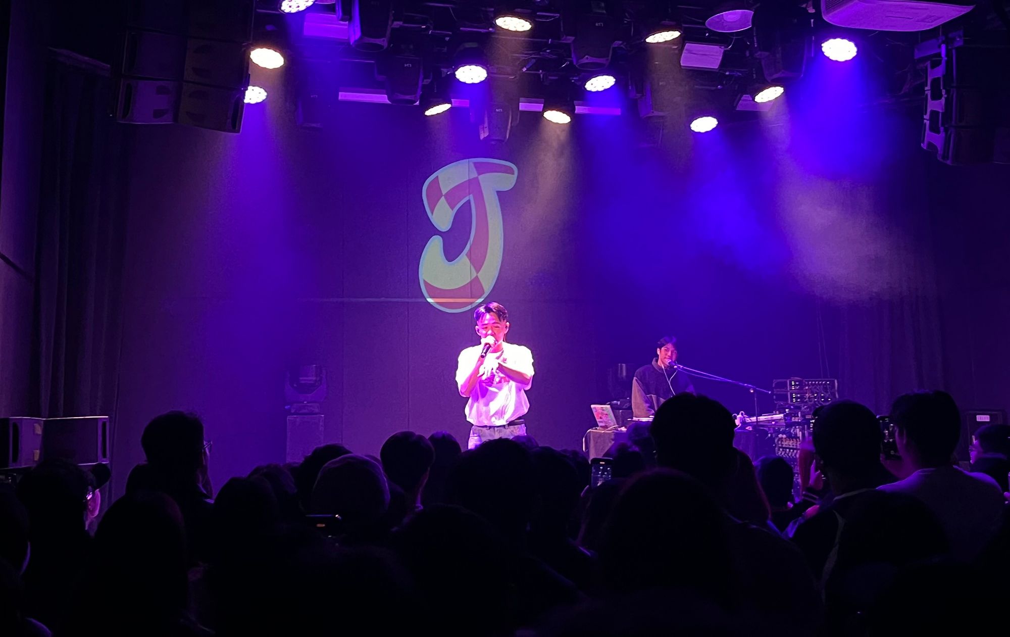 rapper with microphone in front of giant J, next to him is a DJ